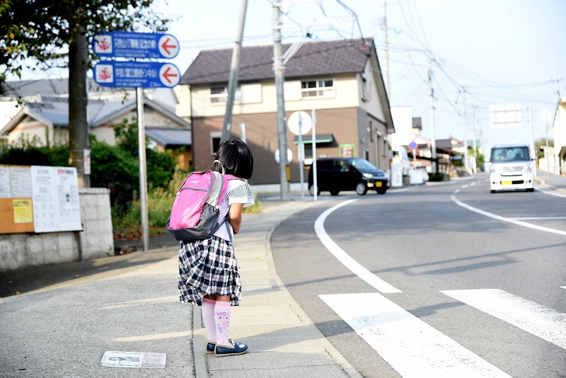 道路の端で車におじぎをする女の子の様子