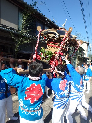 祭りのハッピを着た担ぎ手が神輿を高く担ぎ上げ、練っている様子です。