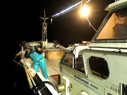 夜中、漁船に灯りをつけて漁をしている様子の写真です。