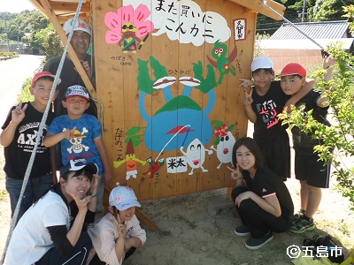 久賀小中学校の児童たちが無人販売所で記念撮影する様子